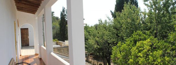 The arched whitewashed porch running along the rooms, looking out over pine and garden green.