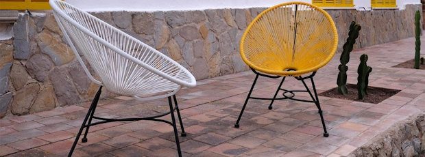 A white and a yellow woven egg-chair on the stone-paved terrace, beside a low rubble-stone wall.