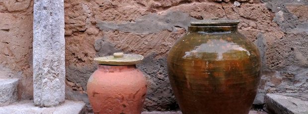Two old terracotta storage urns, one lidded, standing against a weathered rubble-stone wall.