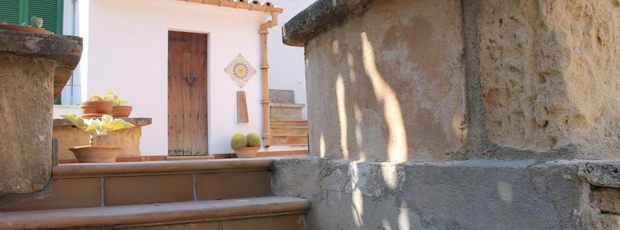 Tiled steps leading up to an open timber door of the hostal, potted plants and a painted ceramic sun on the whitewashed wall.
