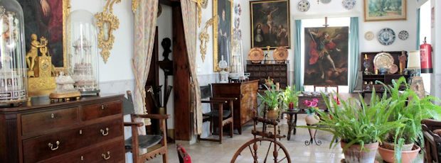 The salon: antique chests and chairs, gilt-framed mirrors and oil paintings, and potted ferns in the old whitewashed room.