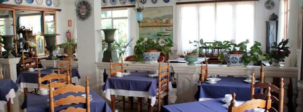 The dining room laid for breakfast: blue tablecloths, wooden ladder-back chairs, and hand-painted blue ceramic plates ranged along the wall.