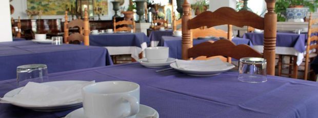 A breakfast place setting close up: a white cup and plate and a glass on the deep-blue tablecloth.